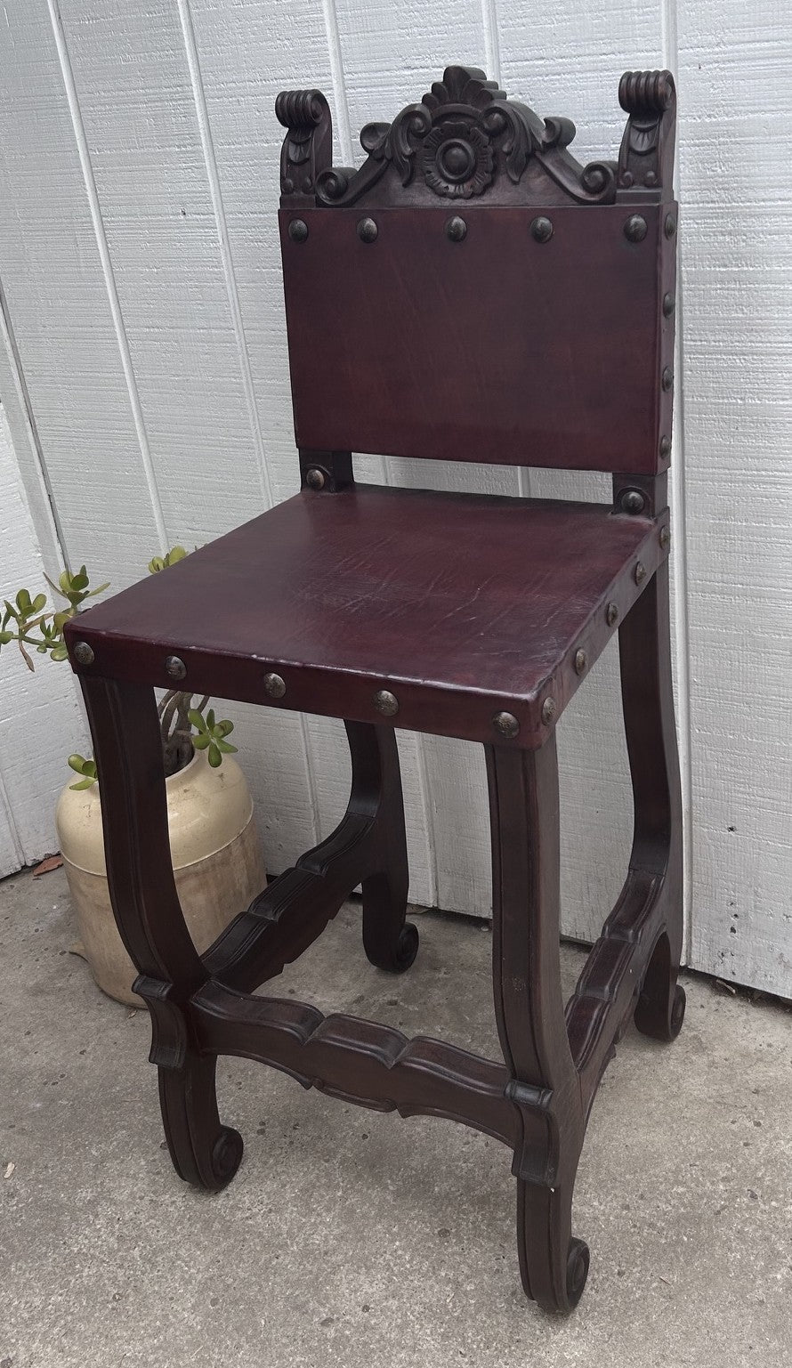 Dark wooden chair with decorative backrest against a white wall.